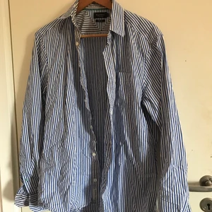 Vit och blå randig skjorta i strl M - Vit och blå randig skjorta slim fit i strl M ifrån märket East West. Skjortan är i bra kvalite och skick och passar perfekt som exempelvis overshirt nu till sommaren. Köparen står för frakt alt mötas upp i Lund
