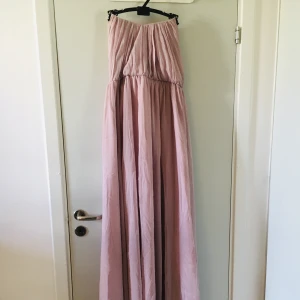 Axelbandslös klänning - Fin långklänning från Gina tricot   Stängs med dragkedja i ryggen.  En hyska som ska sitta ovanför dragkedjan saknas. Enkelt att ordna för den händiga