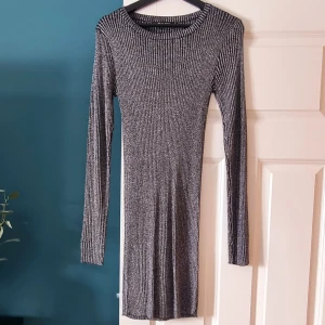 Glittrig klänning  - Långärmad figurnära klänning i glittrigt tyg. Oanvänd. 