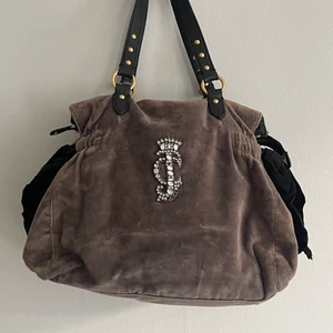 Juicy couture velour väska - Mellanstor Juicy Couture väska i grå velour, fint skick men några år gammal! Alla rhinestones på JC-trycket kvar, något solblekt på vissa delar av gråa velouren, 37x28cm med rosetter på sidorna.