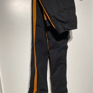 Kostymbyxor - Svarta med orange remsa längs benet stl 32 men stora i storleken 