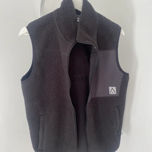 Väst - Svart väst med fickor i sidorna och en på bröstet.