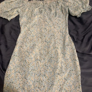 Blommig klänning - Säljer denna blåa blommiga klänning, den är jättefin och fint på, den slutar ungefär vid hälften av låren.