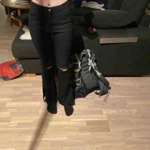 Utsvängda svarta jeans - Ett par svarta jeans med hål i knäna. Det är öppnai sidan på ändorna  på båda sidorna. Dem är bekväma och man kan röra sig i dem. 