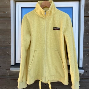 Napapijri flisjacka strl M - Supergo flisjacka som funkar bra som mellanlager. Fin gul färg, sparsamt använd. Storlek 38 (M). Går en bit ner över rumpan. Resårsnören i midjan.