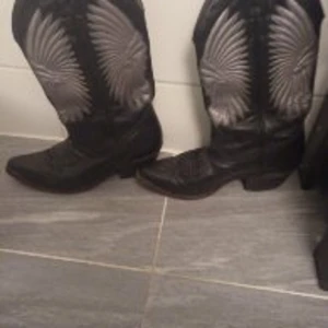 Cowboyboots  - Säljer ett par cowboyboots,snygga sådana. Strl 39,4-40. Svarta med silvrigt mönster, lite mörkbrunt i nyans. stabila och tåliga.