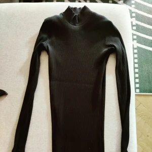 Svart, tight klänning - Tight festklänning med halvpolo, fint ribbad i svart. Längd ca halva låret, beror på din egna längd.