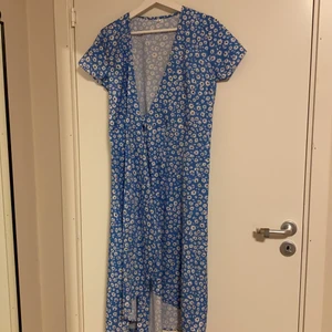Blå klänning  - Blå klänning med vita blommor. Svårt att fota men det finns ett band som man knyter i midjan. Aldrig använd :)