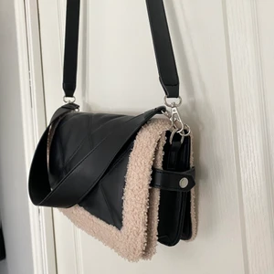 Svart axelremsväska  - Använd ca 2 gånger och säljer då jag inte fått användning för den. Säljs längre inte i butik, men mycket snygg med detaljerna på sidorna! Rymlig och går att spänna ut med knäppen på sidorna, se på bilden ☺️ ordinarie pris är 349kr