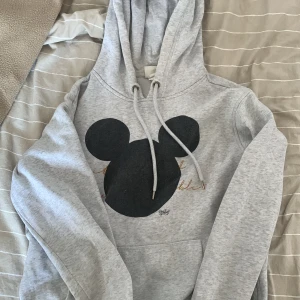 Grå hoodie  - En grå hoodie med micky mousse på. Det står även Disney på den under micky mousse