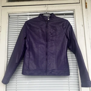 LILA LÄDERJACKA - Lila läderjacka (vegansk läder) säljes. Supermjuk, inga skador eller dylikt. Kan skicka bild på hur den sitter. Pyttelite lukt från vinden, dock försvinner det om man vädrar. Inget som påverkar eller märks av alls. Strl: L, passar dock S/M. 
