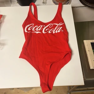Coca cola body storlek s - En body från coca cola med knäppning vid gren. Storlek S