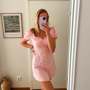 Rosa klänning - Klänning från Nelly med rosa mönster och knappt, väldigt fin form och skön att ha på sig. Går att ha axlarna off shoulder också om man vill det. Är lite skrynklig för har inte strukit den. 