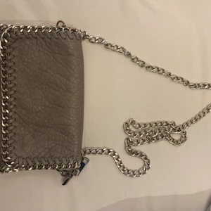 tiamo väska - säljer nu denna jättefina gråa tiamo väskan som inte inte kommer till användning tyvärr. tappat färg på sidan av kedjan men annars i bra skick! köparen står för frakten💗