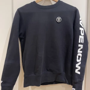 Aape Sweatshirt - Snygg och stilren sweatshirt från Aape. Tröjan är köpt på Aape i Hongkong och är i väldigt bra skick. Märket på framsidan är avtagbart. Nypris ca. 1000kr.