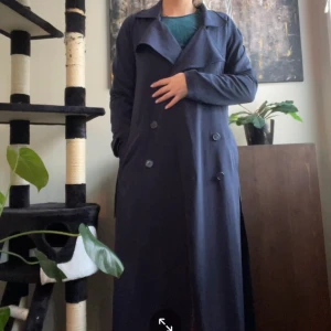 Trenchcoat  - blå Trenchcoat, band och fickor och knappar. Ankellång, knappt anvönd