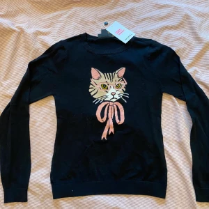 Finstickad kofta med katt XS - Finstickas kofta med katt. Strl  XS. Passar säkert en tonåring så väl som dam. Lapparna kvar men köpt för några säsonger sen. Passar perfekt under en kavaj så väl som till ett par jeans.  96% Bomull, 3% Polamid, 1% ”Annat material”