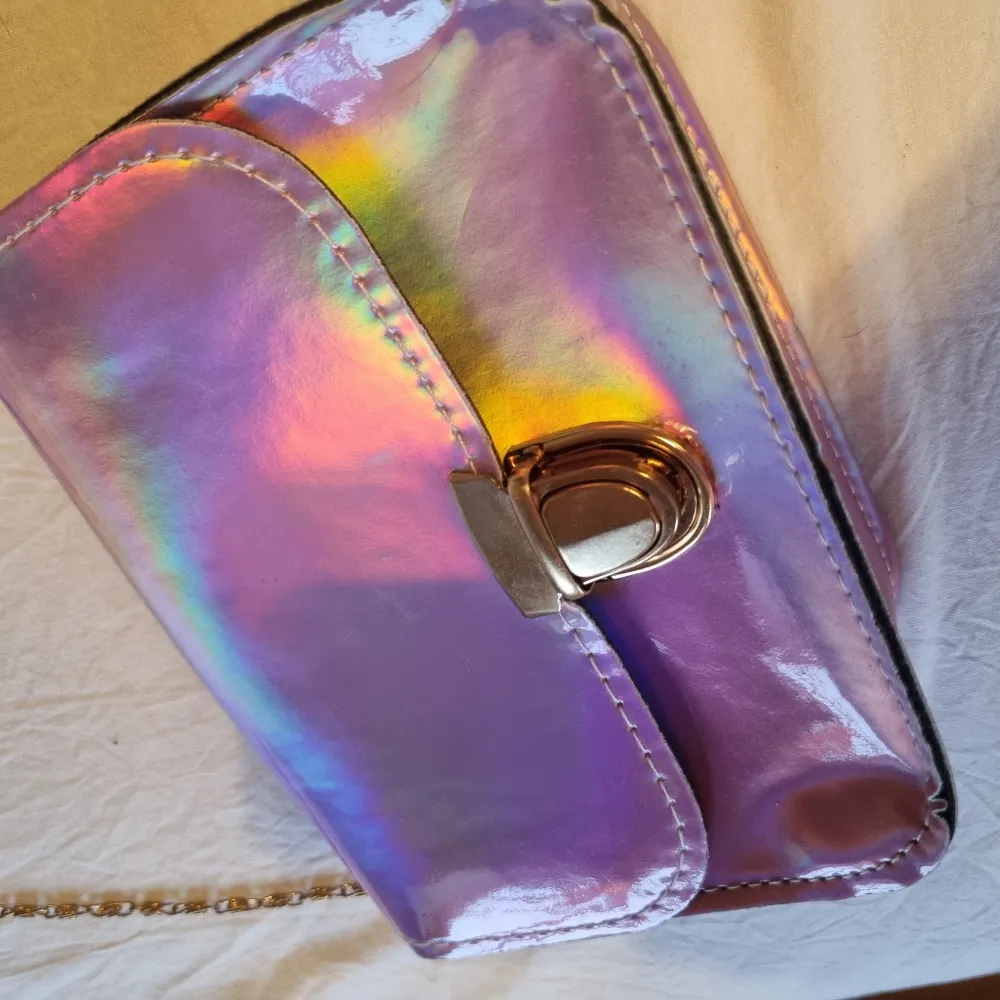 Rosa/lila/holografisk handväska med guldfärgat spänne och kedja. Med fake-läder på insidan. Köpt på Shein, endast använd någon enstaka gång.. Väskor.