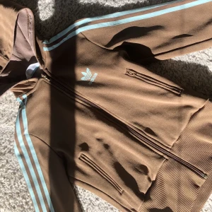 Adidas zip up - En as cool unik adidas zip up, säljer pga av att den inte kommer till användning. Den ör brun med turkosa detaljer, Skicket är som nyskick💕