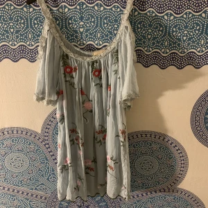 Flowy blommig klänning - Blommig kort klänning med öppna axlar, använd en gång. Blommorna är broderade. Storleken är S/M.