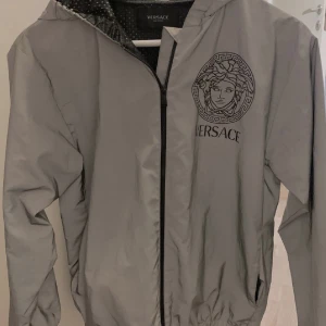 Versace jacka - Versace reflex jacka som lyser i mörkret och byter färg när det regnar. Unisex! Köpt på NK i Stockholm för 5000:-, storlek 152. Passar mig perfekt jag är en XS. Jag säljer den för endast 1200:-