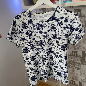 Blommig blå t-shirt stl S - En väldigt somrig och ganska tunn tröja som är perfekt för lite varmare väder. Samma mönster på hela tröjan. Storlek S och märket är The Tailorino Club. Bra skick.