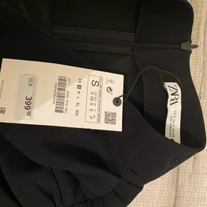 Lång kjol från zara  - Svart lång kjol med slits från zara. Fin drapering på ena sidan och kjolen är i kostym-material. Aldrig använd med lapp kvar. Dragkedja där bak. 