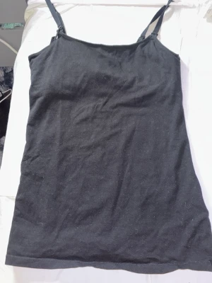 Svart linnetopp från H&M Mama - En enkel svart linnetopp från H&M Mama med smala axelband. Toppen är ärmlös och har en rak passform, perfekt för att styla lager på lager. Tillverkad i mjuk bomull för skön känsla hela dagen.