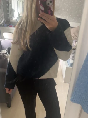 Stickad tröja med svart och vit design - Snygg stickad i vitt och svart. Tröjan har rund halsringning och långa ärmar. Mjuk och skön, perfekt för kyligare dagar. Passar till både jeans och kostymbyxor för en trendig look.