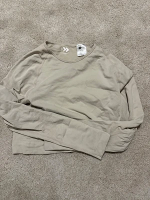 Tränings tröja  - Säljer en stilren beige långärmad tröja från 157. Tröjan har rund halsringning och är tillverkad i ett mjukt, stretchigt material som passar perfekt till lager-på-lager. Enkel och clean design utan tryck eller mönster.
