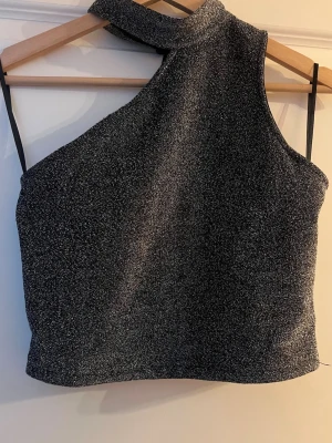 Glittrig oneshoulder topp  - Glittrig svart/silver oneshouldertopp med knäppning i nacken