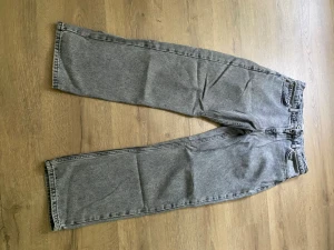 Grå raka jeans med hög midja - Säljer ett par grå jeans med rak passform och hög midja. Jeansen har klassiska fem fickor och är tillverkade i ett kraftigt denimtyg. Perfekta för en avslappnad och trendig look.