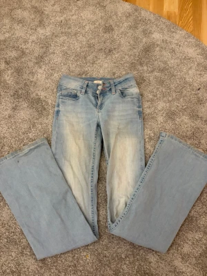 Ljusblå bootcut jeans från Nelly - Säljer ett par ljusblå bootcut jeans med snygg broderad detalj i rött på bakfickorna. Storlek 32 , lite söndrigt längst ner som man kan se. Tvättas innan de skickas! nypris-699