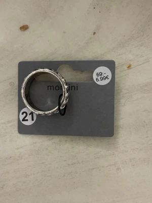 Silverfärgad ring med mönster Montini  - Snygg silverfärgad ring från Montini med ett detaljerat, snirkligt mönster runt hela ringen. Ringen har en bred design och en lätt antik finish som ger den en cool vintagekänsla. Perfekt för dig som gillar statement-smycken och vill sticka ut.