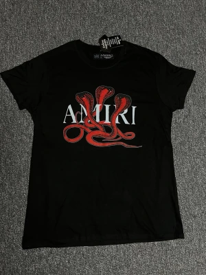 Svart Amiri t-shirt med röd orm - Svart t-shirt från Amiri med ett stort tryck av en röd orm och vit text på bröstet. Klassisk rund hals och korta ärmar. Perfekt för dig som vill sticka ut med en cool och edgy look.