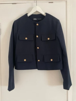 Zara kavaj - Stilren mörkblå kavaj från Zara med snygga guldknappar framtill. Rak, något kortare modell med rund halsringning och långa ärmar. 