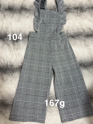 Grå-rutig byxdress med volang - Byxdress i grått rutigt tyg med vida ben och volangprydda axelband. Hög midja och klassisk rutig design ger en trendig och stilren look. Perfekt för dig som gillar detaljer och mönster.🌸 Fint använt skick. Storlek 104 