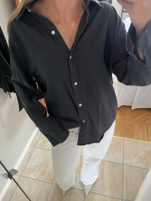 Mörk oversized skjorta - Svart oversized skjorta med vita knappar. Skjortan är i mjuk bomull och har långa ärmar. Skulle uppskatta storlek L. Sitter även snyggt på herr! 