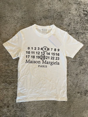 Maison Margiela T-shirt  - Säljer denna fina helt oanvända vita tröjan med  MM6 tryck. Tröjan är i storlek S. Men lite liten i storleken så passar nog också XS. Köpt från Vinted. Perfekt nu inför sommaren! Hör av er ifall ni har några frågor! ⚜️⭐️⛱️