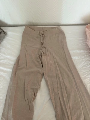 Beige vida mjukisbyxor med dragsko - Säljer ett par beige mjukisbyxor med vida ben och dragsko i midjan. Byxorna är tillverkade i ett mjukt och stretchigt material som känns skönt mot huden. Perfekta för en avslappnad och chill stil. Oanvänd 