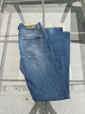 Nudie Jeans Grim Tim – Org. Slub Ecru Embo (W32/L32) - Säljer ett par riktigt sköna och stiliga Nudie Jeans i den omtyckta modellen "Grim Tim". Tvätten heter "Org. Slub Ecru Embo" och ger byxorna en perfekt, insliten look med snygga skuggningar och detaljer. Modellen har en smal passform med normalhög midja, och tack vare att de är gjorda i 98% ekologisk bomull och 2% elastan är de både följsamma och superbekväma att ha på sig hela dagen.  Modell: Grim Tim.  Tvätt: Org. Slub Ecru Embo.  Storlek: W32 L32.  Material: 98% ekologisk bomull, 2% elastan 