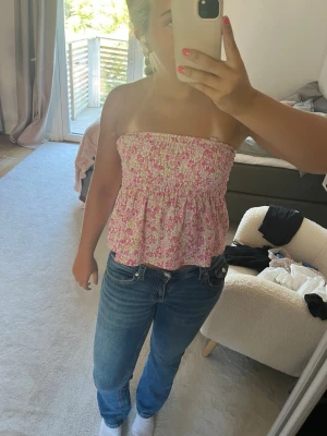 Blommig bandeau tubtopp i rosa och vit - Säljer en söt bandeau tubtopp med blommigt mönster i rosa och vitt. Toppen är ärmlös och har en smockad överdel som ger en bekväm passform. Perfekt för varma dagar och enkel att styla med jeans eller kjol. Men snören tillkommer-sista bilden.  Knappt använd