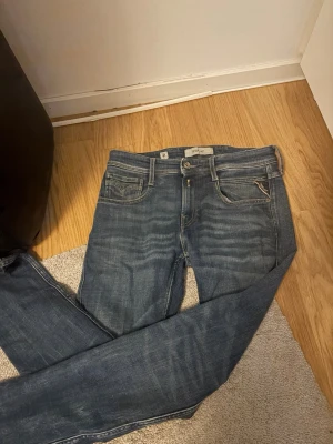 Blå raka jeans med klassisk look - Snygga blå jeans med raka ben och klassisk femficksdesign. Jeansen har ljusa slitningar och kontrastsömmar, samt en liten ficka med V-detalj. Perfekta för en avslappnad och trendig stil. Materialet är denim i bomull.