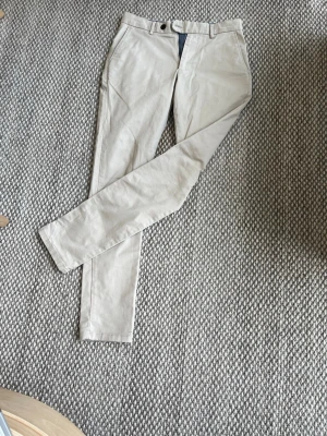 Beige chinos med raka ben - Snygga beige chinos med klassisk passform och raka ben. Byxorna har bälteshällor, knapp och dragkedja framtill samt sidofickor. Perfekta för en stilren och avslappnad look.