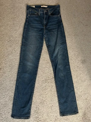 Levi's 724 High Rise Straight Jeans - Säljer ett par klassiska blå Levi's 724 High Rise Straight jeans i storlek 27. Jeansen har hög midja, raka ben och fem fickor. Knappt använda och i fin kvalité!