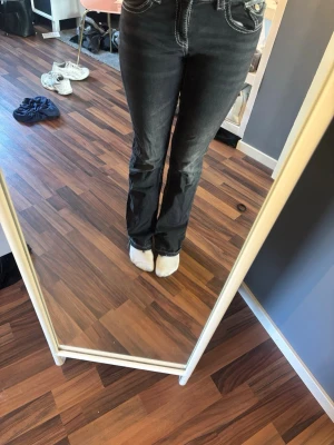 Svarta bootcut jeans med vita sömmar - Säljer ett par svarta bootcut jeans med tydliga vita kontrastsömmar. Jeansen har klassisk femficksmodell och knappstängning. Materialet är denim och passformen är något utsvängd nedtill. Perfekta för dig som gillar en retroinspirerad look.