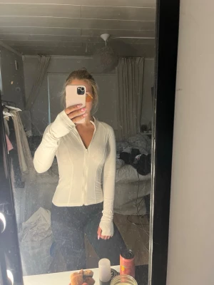 Tränings tröja från Gina  - Säljer en vit långärmad topp med dragkedja framtill. Toppen har en slim passform och är tillverkad i ett stretchigt material som sitter snyggt på kroppen. Inte använd många gånger och i fint skick!