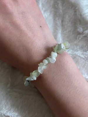 Elastiskt armband med ljusa stenar - Armband med oregelbundna pärlor i ljusgrön och vit ton. Pärlorna är av polerade stenar och sitter på en elastisk tråd som gör det enkelt att ta på och av 😊