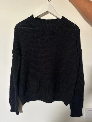 Svart stickad tröja från 157 - En svart stickad tröja från 157 med rund halsringning och ribbade muddar vid ärmslut och nederkant. Tröjan har en enkel och klassisk design som passar perfekt till alla outfits. Materialet är mjukt och bekvämt.