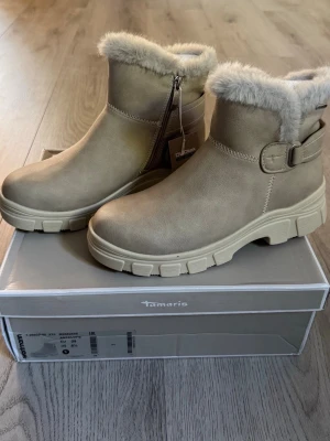 Tamaris Vinterboots - storlek 39 - Tamaris vinterboots – strl 39  Snygga och stilrena vinterboots från Tamaris!  • Storlek: 39 (EU) • Färg: beige/taupe (Antelope) • Varmt och mjukt foder med pälsdetalj upptill • Praktisk dragkedja på sidan • Stabil och kraftig yttersula med bra grepp • Snygg detalj med spänne på sidan • Modellnummer: M2682545 / 1-26825-45 375  Skorna är helt nya & säljs tillsammans med originalkartongen.  Perfekta för höst och vinter – både snygga och bekväma! ✨  Pris: 550kr
